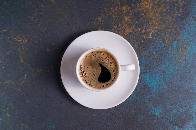 A cup of black coffee on blue table, top view.