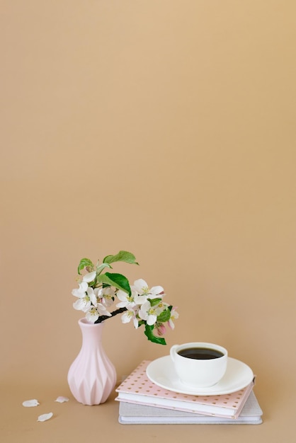 Cup of black coffee books and a sprig of apple blossoms on a beige background with a copy space