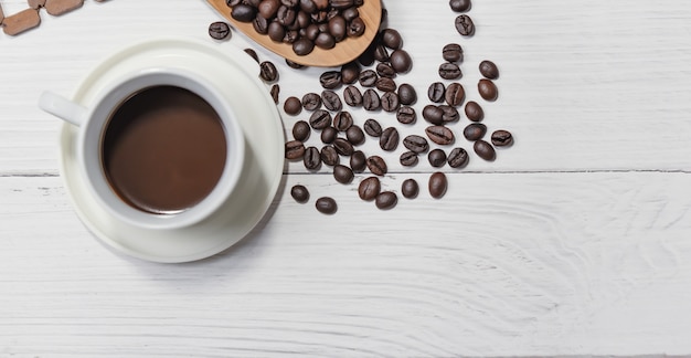 Cup of black coffee  and coffee beans good essentials on white wooden table. Top view.