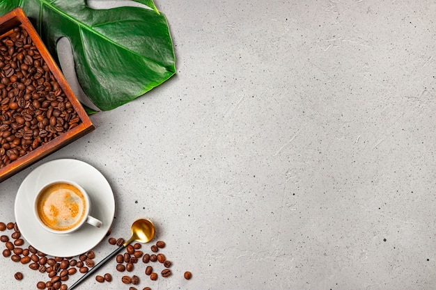 Cup of black coffee, coffee beans in the wooden box and monstera leaf on the gray concrete background