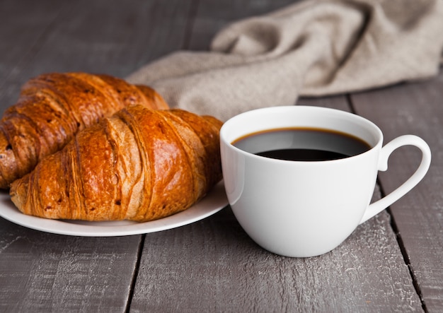 Cup of black coffee and croissant for breakfast on wooden surface