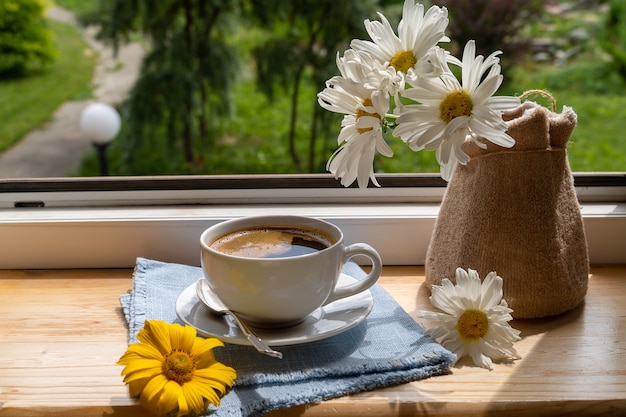 太陽の光の下の窓辺にある一杯のブラックコーヒーと庭の花、そして美しい花。