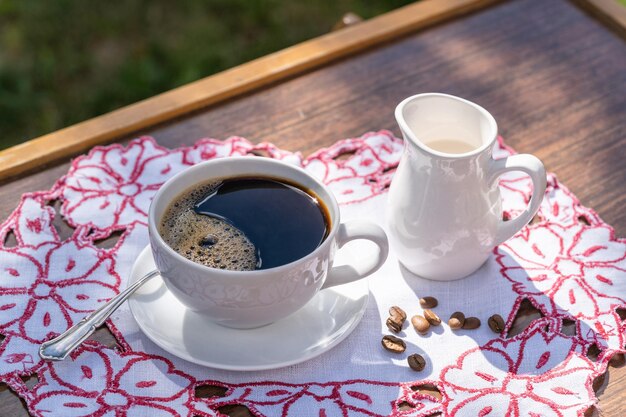 A cup of black coffee and milk on a table on natural defocused background in garden