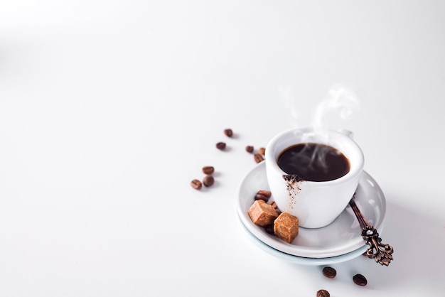 Чашка черного кофе на блюдце с коричневым сахаром на белом фоне