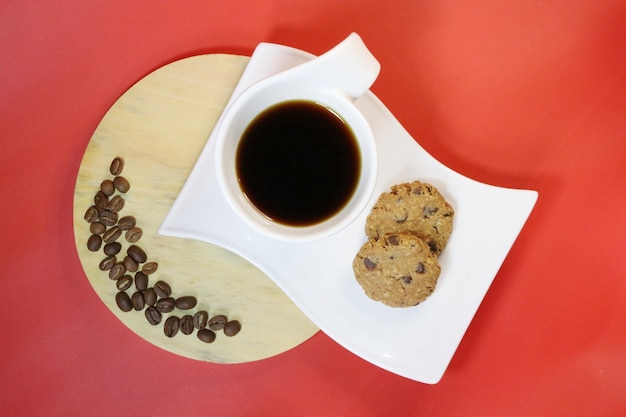 A cup of black coffee and two chocolate cookies on bright red background Flat lay concept