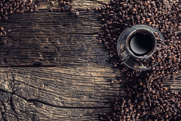 cup of black coffee with beans on wooden table.