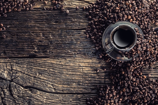 Cup of black coffee with beans on wooden table.