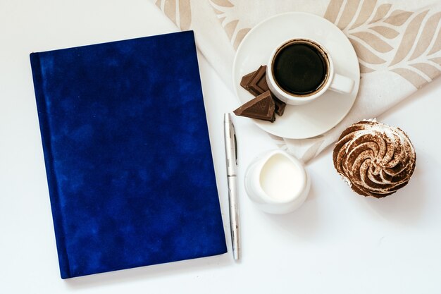 A Cup of a black coffee with chocolate and cupcakes and a blue Notepad