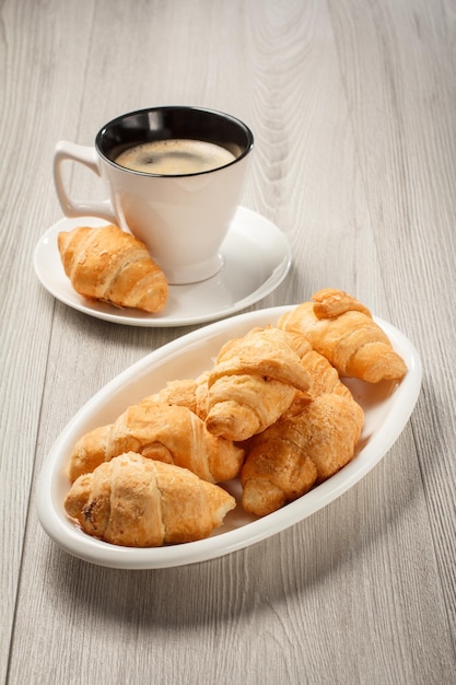 Cup of black coffee with saucer fresh croissants on white porcelain dish