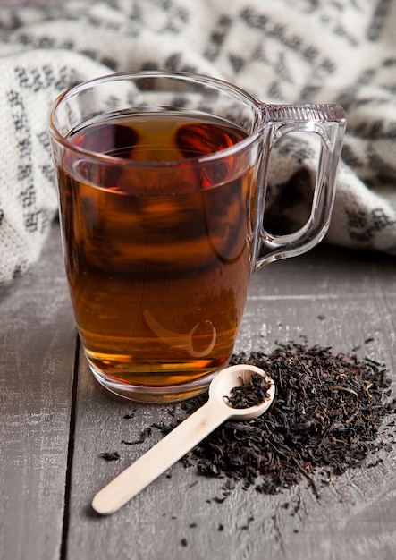 Cup of black healthy tea scarf and loose tea on wooden surface