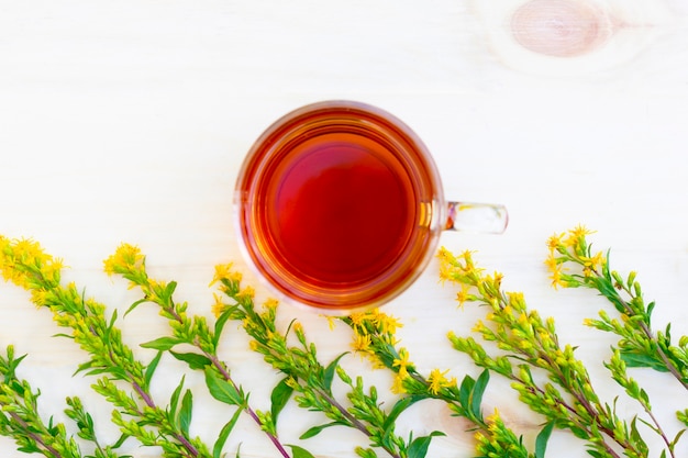 The cup of black herbal tea with branches of hypericum or tutsan on wooden table