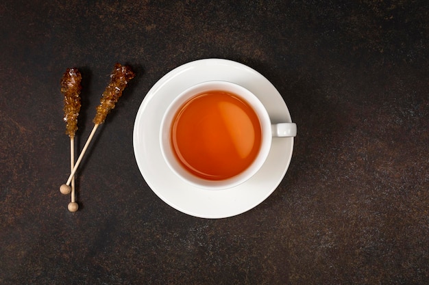 A cup of black tea and caramel sugar on brown background Top view Copy space