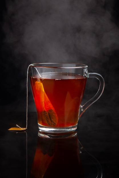 Cup of black tea with steam on a dark 