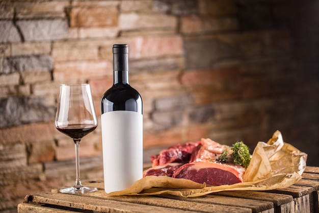 Cup and a bottle of red wine and raw beef steak on wooden table.