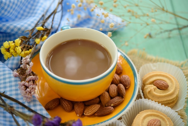 A cup of cafe latte and cookie with almonds on wooden table.