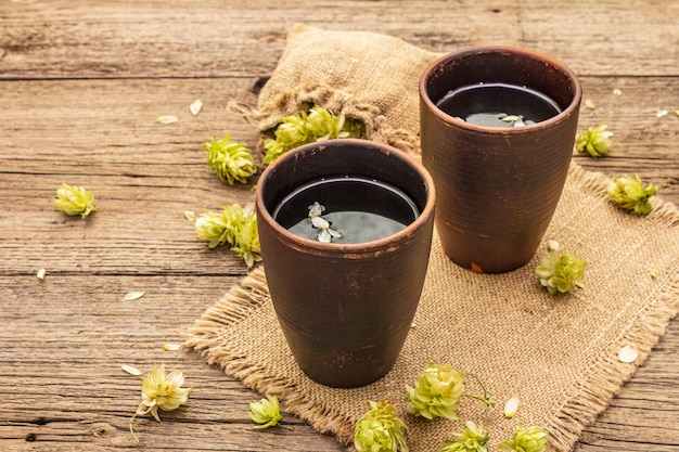 Cup of calming herbal tea with fresh wild hops. Hops cones in sack on vintage boards