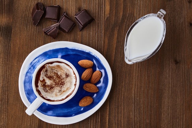 Cup of cappuccino almonds chocolate and milk in a glass milk jug on a dark wooden table