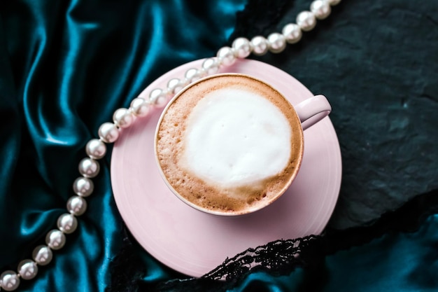 Cup of cappuccino for breakfast with satin and pearls jewellery\
background organic coffee with lactose free milk in parisian cafe\
for luxury vintage holiday brand