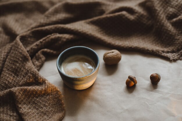 Cup of cappuccino on a brown paper texture background with cozy warm plaid walnuts and acorns