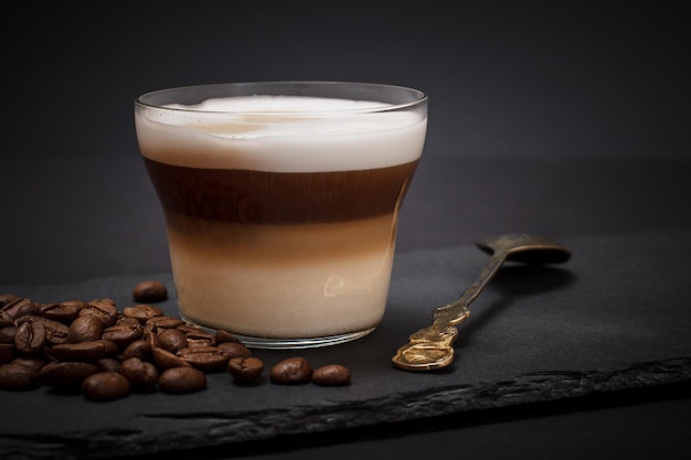 Cup of cappuccino, coffee beans and spoon on black background.