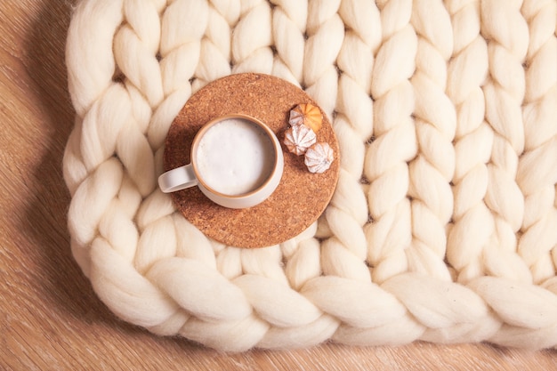 A cup of cappuccino and cookies on the background of blanket of thick yarn. The atmosphere of homeliness and comfort
