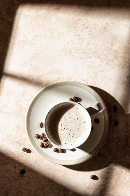 A cup of cappuccino or latte with coffee beans close up with shadows on beige background Top view copy space