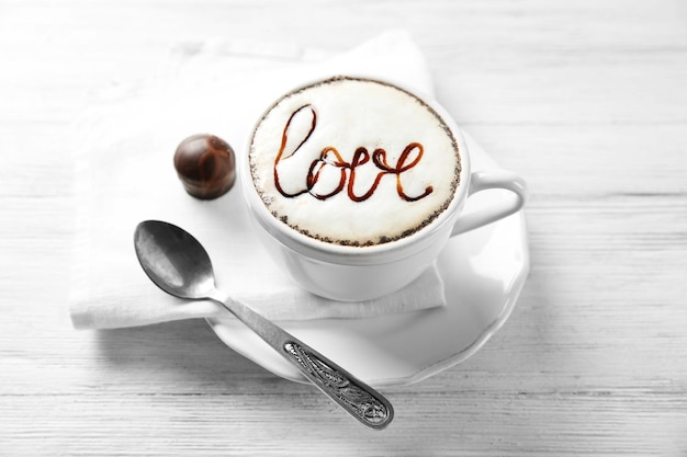 Photo cup of cappuccino with chocolate syrup and candy on light wooden table