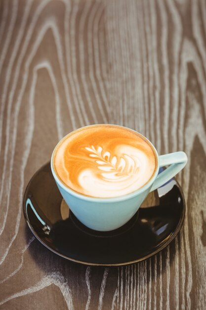 Cup of cappuccino with coffee art on wooden table at coffee shop