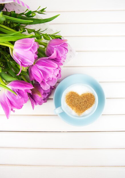 Cup of cappuccino with a heart shaped symbol and purple tulips on a wooden background