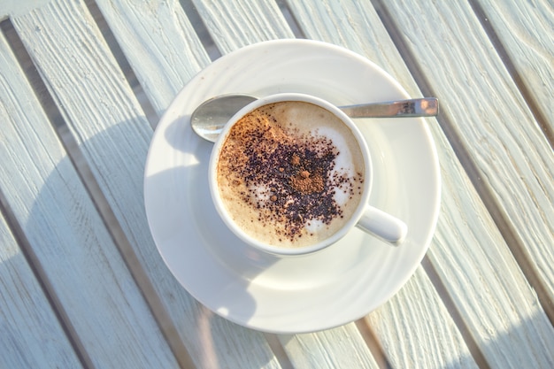 Cup of cappuccino with latte art on wooden white table. top view.