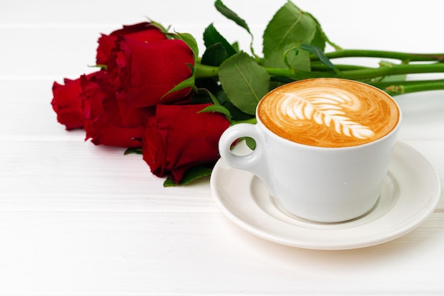 Cup of cappucino with art and bouquet of roses on wooden table