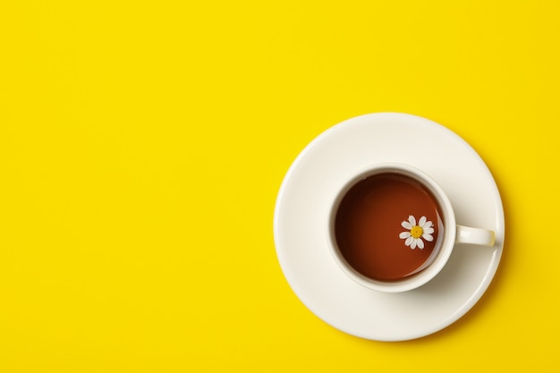 Cup of chamomile tea on yellow background