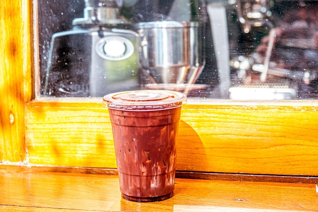 A cup of chocolate smoothie sits on a window sill.