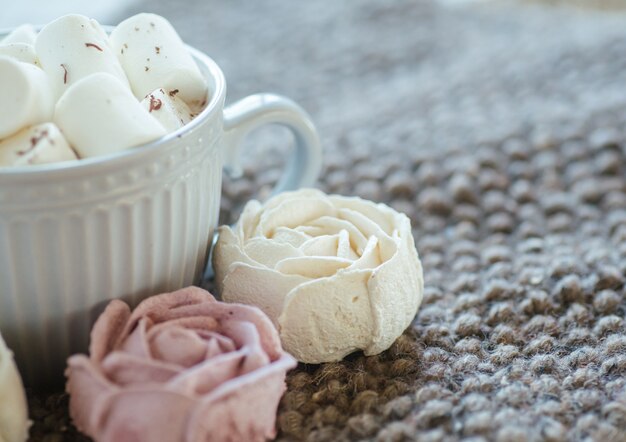 A cup of cocoa or chocolate next to a rose-shaped marshmallow.