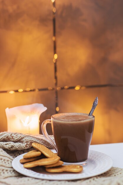 Una tazza di cacao e biscotti su un piatto bianco su un tavolo bianco e una sciarpa lavorata a maglia