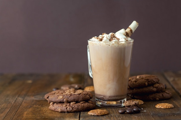 Cup of cocoa with marshmallows and chocolate chip cookies on dark wooden background.