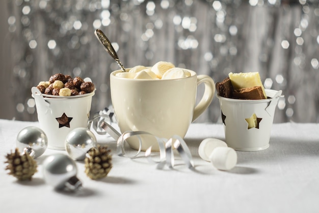A cup of cocoa with marshmallows and chocolate in the New Year Christmas table setting on a shiny background