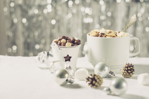 반짝이는 배경에 놓인 새해 크리스마스 테이블에 마시멜로와 옥수수 공을 넣은 코코아 한 잔