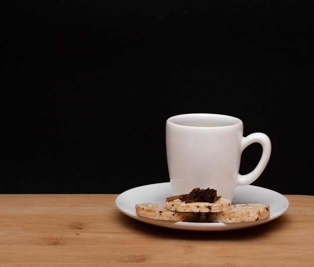 Tazza di caffè accanto a biscotti vegani di riso con una gelatina in cima sotto il tavolo di legno