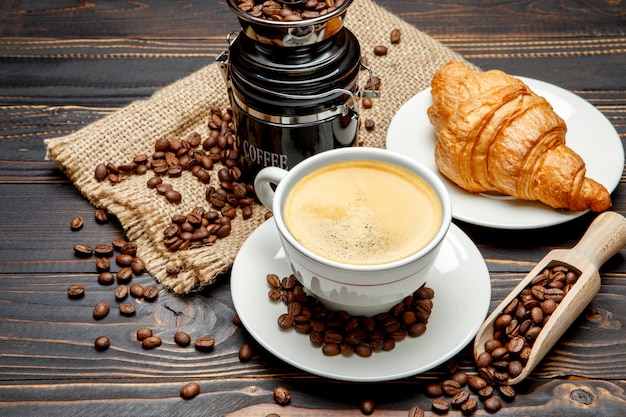 Cup of coffe and croissant on wooden background