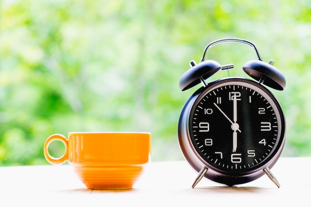 Cup of coffee and alarm clock on a Desktop from wooden plank.