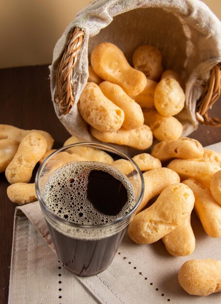 Photo cup of coffee in a american glass typical cup from brazil polvilho biscuit falling from a basket into table in the background