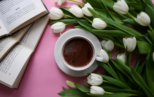 Cup of coffee among arranged white tulips top view