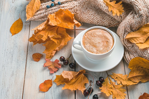 A cup of coffee autumn foliage and a cozy sweater on a beige background