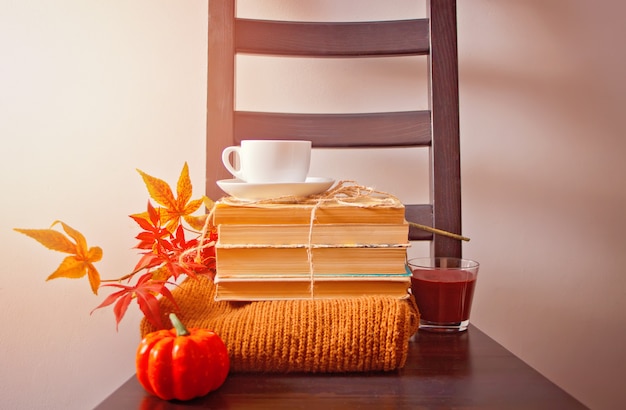 Tazza di caffè, foglie di autunno, zucca, libri e maglione sulla sedia di legno.