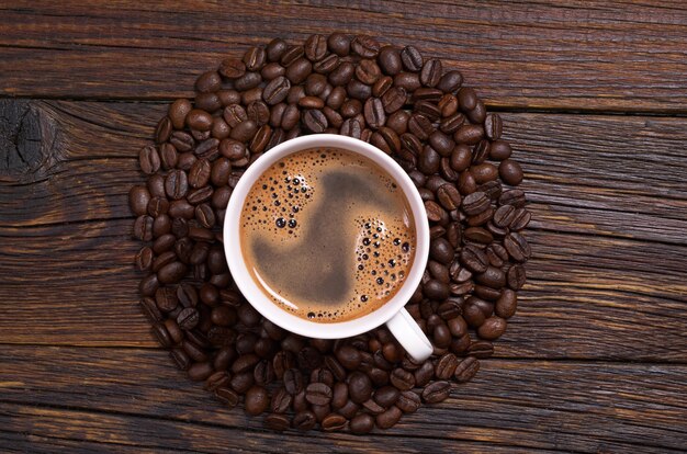 Cup of coffee and beans arranged in shape of a circle on dark wooden background, top view