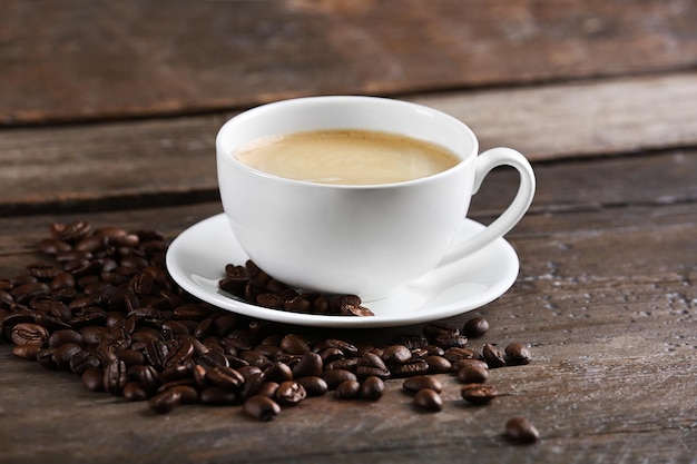 Cup of coffee and beans on wooden table close up