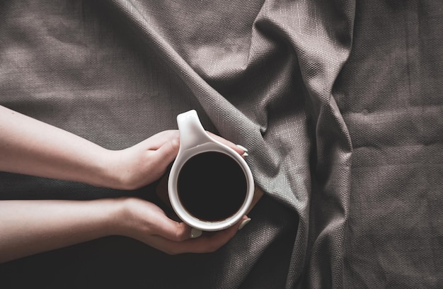 Cup of coffee in bed in female hands flat lay