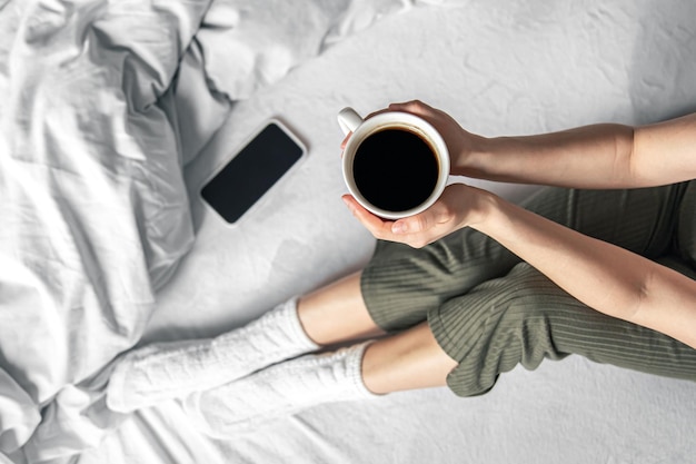 Cup of coffee in bed in female hands top view