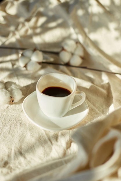 Cup of coffee in bed with cotton flowers morning mood organic\
and natural linen cotton textile bedclothes copy space